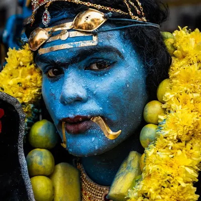 A close-up portrait of a devotee painted blue to represent a deity, his intense gaze and traditional adornments showcasing the festival's transformative power.