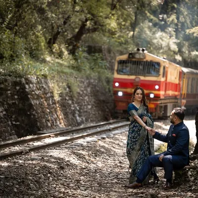 A beautifully composed shot with the couple seated by the tracks as the Shimla toy train approaches, creating a sense of journey and timeless romance.