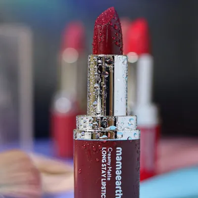 A close-up of a Mamaearth matte lipstick, covered in fine water droplets, to emphasize its rich color and hydrating quality against a soft, dreamy background.