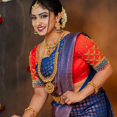 A classic studio portrait of a model in a royal blue silk saree with a contrasting embroidered red blouse. Her direct, smiling gaze and the clear visibility of the complete jewelry set make this a perfect image for a festive campaign.