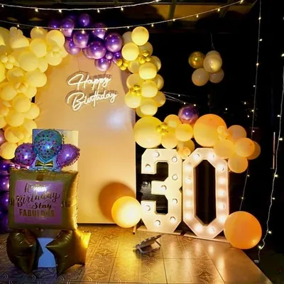A 30th birthday bash done in style. This setup features a 'Happy Birthday' neon sign, marquee numbers, and a dramatic purple and yellow balloon arch, creating a vibrant backdrop for a milestone celebration.