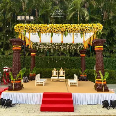 A magnificent traditional mandap for a daytime wedding, featuring ornate pillars, a canopy of yellow marigolds, and elegant seating for the couple and their families.
