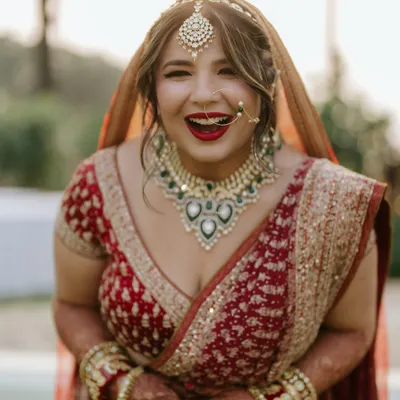 A classic red bridal look complete with a bold red lip and a traditional nath. Her joyful laugh shows she feels as amazing as she looks. This is a timeless choice for any bride.