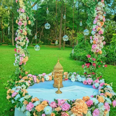A romantic outdoor photo booth for a wedding or engagement. This setup features a square floral frame with hanging glass globes, set against a beautiful green lawn.