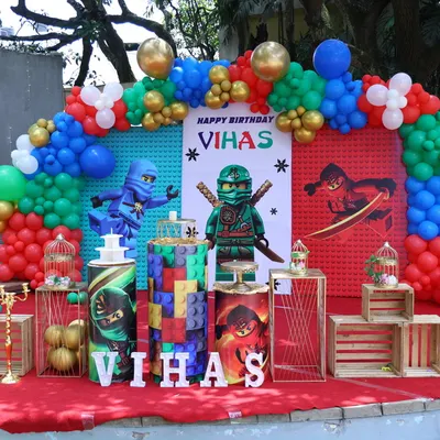 This is a full-scale Ninjago-themed birthday stage. The rental package includes the character backdrop, colorful balloon arch, and themed cylindrical plinths for the cake display.