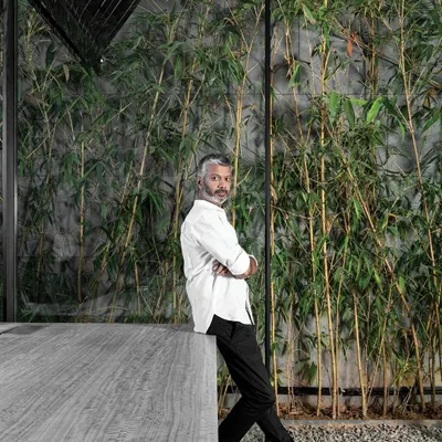 A portrait of me, Ar. Sumit Dhawan, in my element. Here I am leaning against a concrete table with a backdrop of bamboo, reflecting my design philosophy of blending raw, modern materials with natural elements.