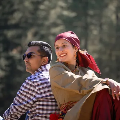 A relaxed portrait of the couple sitting back-to-back, dressed in a mix of traditional and modern attire, symbolizing the beautiful blend of their personalities.