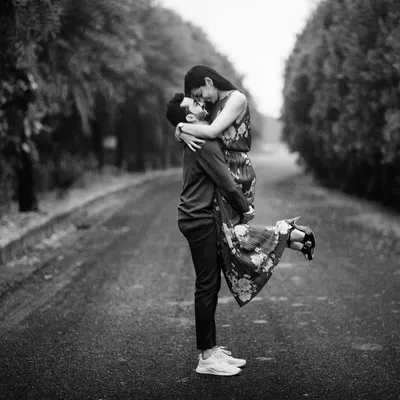 A classic black and white shot of him lifting her up on an empty road. The composition creates a feeling of romance and timelessness, like a scene from an old movie.