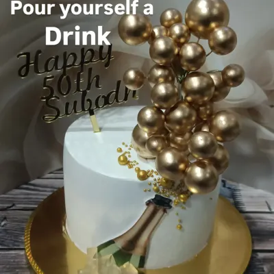 A fun and celebratory cake for a 50th birthday. This design features a champagne bottle popping with golden spheres, creating a sense of bubbly excitement.