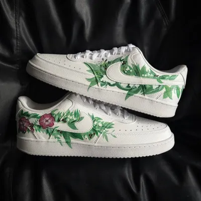 A pair of white Nike Court Vision sneakers adorned with a hand-painted design of fresh green leaves and pink flowers.