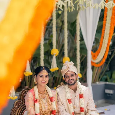 A happy portrait of the bride and groom at their South Indian wedding. The mandap is decorated with traditional flowers, creating a beautiful and authentic setting for their ceremony.