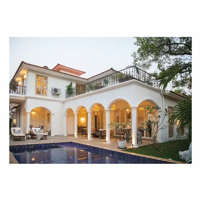 An exterior view of the 'Sand Tales' villa in Goa, designed as a home away from home. The classic architecture with its arched verandah and poolside setting creates a perfect environment to unwind and find solace.