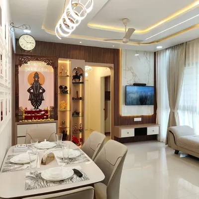 An open-plan living and dining area where the design flows seamlessly. The space includes a modern dining set under a statement chandelier, with the TV and pooja unit visible in the background, creating a unified look.