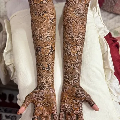 A complete bridal henna design that extends up the full arm. The patterns are a mix of floral motifs, paisleys, and intricate net-work, creating a classic and rich look for the bride.