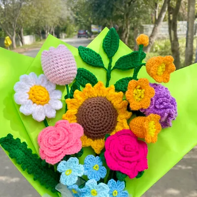 This colorful mixed flower bouquet looks so beautiful in the natural sunlight. It has a sunflower, roses, a tulip, and other pretty blooms, showing how different handmade flowers can come together to create something truly special.