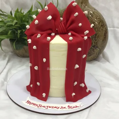 This elegant cake features a dramatic red bow made from fondant, draped over a smooth white ganache base. It's a stylish and modern design that makes a bold statement at any event.