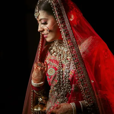 A classic bridal portrait with a red veil, showcasing the bride's intricate jewelry and serene expression against a dark background.