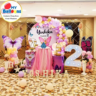 A breathtaking butterfly theme for a second birthday. This setup features a mirrored floor, a central tulle-draped table, large butterfly cutouts, and a pink and purple balloon arch, creating a truly magical atmosphere.