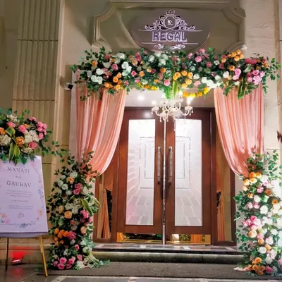 A grand and welcoming entrance for Manasi and Gaurav's wedding at the Regal. The doorway is framed by a lush arch of pastel flowers and soft drapery, with a personalized welcome sign to greet guests.