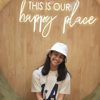 A happy young client posing in our signature photo spot. The "happy place" sign is a favorite for capturing joyful moments.