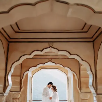 A beautifully symmetric shot using the layered arches of a Jaipur palace to frame the couple. This intimate forehead-to-forehead pose creates a sense of unity and peace amidst the grandeur.