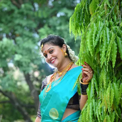 A beautiful outdoor portrait of a woman in a traditional silk saree. Natural light brings out the rich colors of the attire and the warmth of her smile, perfect for any family function album.