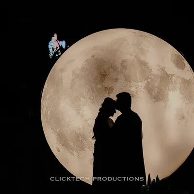 A stunning silhouette of a couple embracing in front of a giant, illuminated moon prop, creating a magical and romantic night-time photo.
