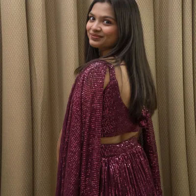 An over-the-shoulder shot from an indoor portfolio session. This pose highlights the back design of the sparkly magenta lehenga.