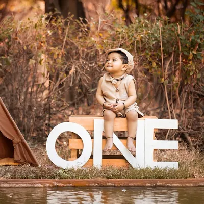 An outdoor first birthday shoot with a rustic, adventurous theme. The 'ONE' sign, teepee, and natural setting create a beautiful backdrop for celebrating this special milestone.
