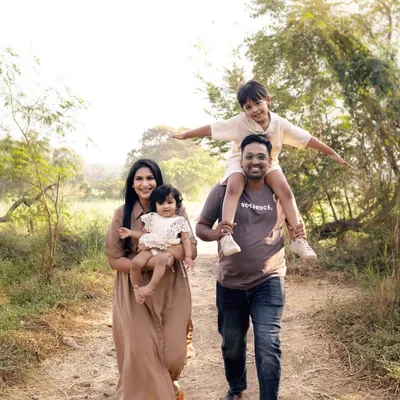 A family takes a walk through a sunlit path, son on his father's shoulders, full of joy. Our outdoor picnic sessions are about capturing your family's adventure.