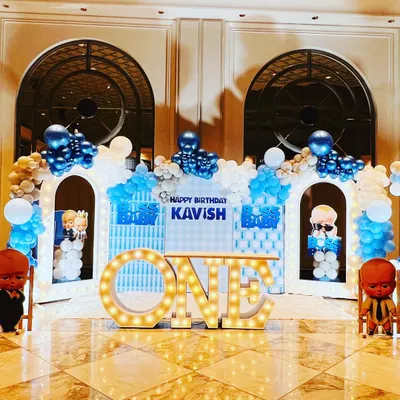 A complete Boss Baby themed stage for a first birthday, featuring character cutouts, city skyline backdrops, and large light-up "ONE" letters.