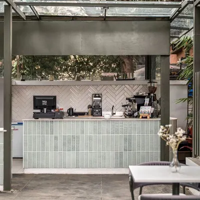 The coffee bar at Kana Cafe, featuring pastel green subway tiles and a white herringbone backsplash. This area is the heart of the cafe, designed with a chic and vibrant appearance to welcome patrons.