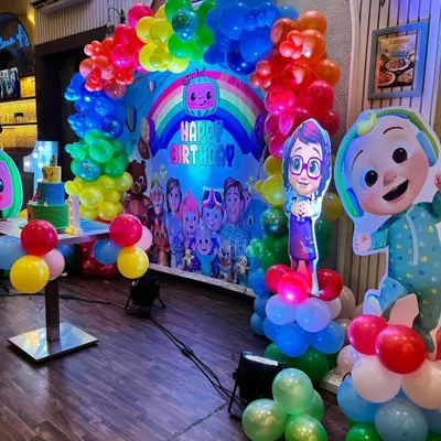 A vibrant Cocomelon theme party setup featuring a rainbow balloon arch over a backdrop filled with all the favorite characters.