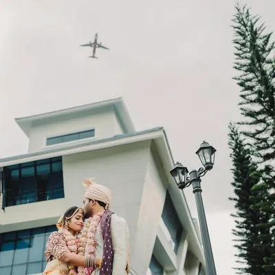 A unique and symbolic shot of the couple in a tender embrace outdoors, as an airplane flies overhead, signifying their journey together.