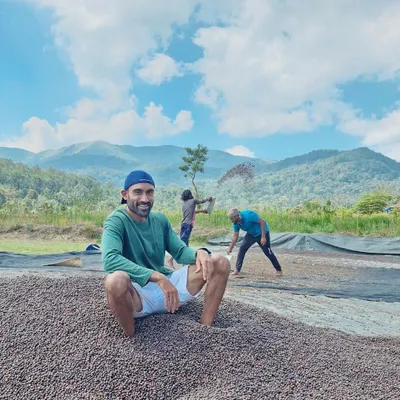 This is what hands-on looks like. I'm sitting on a fresh pile of our Robusta coffee beans as they begin the drying process, a critical step in developing their flavor. You can see the hard work happening right here, with the mountains as our constant backdrop.