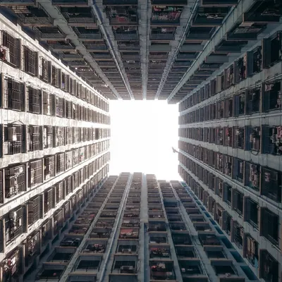 A worm's-eye view looking straight up at the sky, perfectly framed by the repeating patterns of a dense residential building. This shot creates a feeling of being enclosed by the city's vertical growth, a classic Hong Kong-style "monster building" perspective.