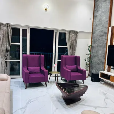 A view of the living room showcasing the vibrant purple wingback chairs that add a pop of personality. The space is designed with high ceilings and large windows to maximize natural light and connect with the outdoors.
