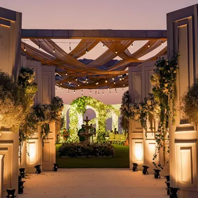 The magical transition from day to night at this white wedding in Goa. The grand entrance, illuminated against the twilight sky, leads to a garden wonderland where the celebration is just beginning.
