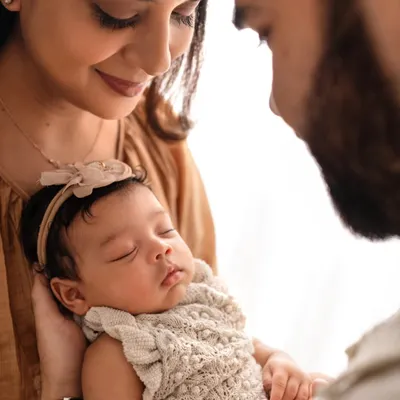 A different angle from a newborn family session, focusing on the parents' loving gaze upon their sleeping baby. These soft, warm images are perfect for remembering those early days.
