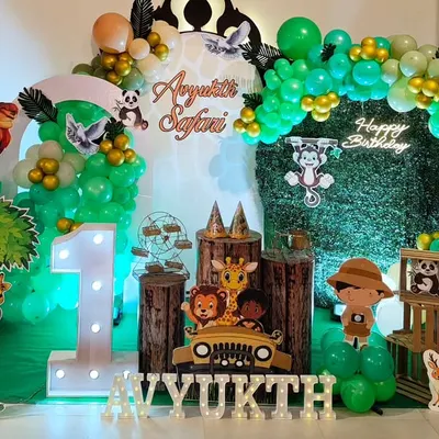 A complete jungle safari setup for a first birthday, featuring a grass wall, marquee number '1', animal cutouts, and a green and gold balloon arch.