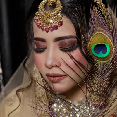 A creative shot featuring a peacock feather. The deep, smoky eye makeup and nude lip create a dramatic and artistic look, perfect for a themed photoshoot.