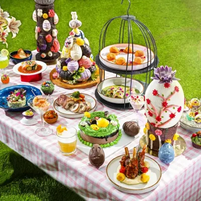 A whimsical Easter brunch fantasy. We created a full tablescape with a pastel checkered cloth, lush green grass, and an abundance of themed treats like bunny cakes and chocolate eggs. This wide shot captures the magical, celebratory atmosphere of the entire spread.