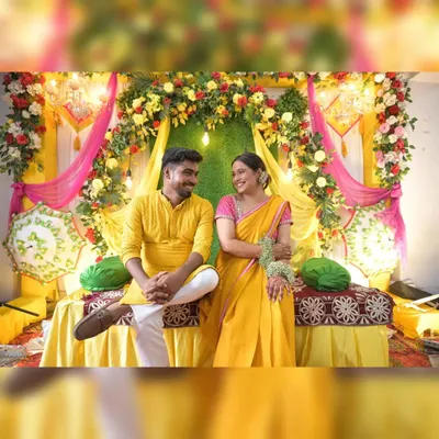 A beautiful couple framed by our classic Haldi ceremony decor. The setup combines a dense floral arch, bright yellow and pink draping, and traditional umbrellas for a complete and festive look.
