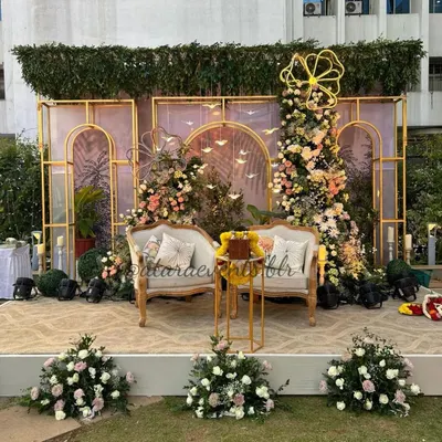 A truly whimsical and elegant baby shower stage. The setup features a stunning floral installation over a gold-arched backdrop, with vintage-style seating, creating a beautiful and sophisticated photo opportunity for the parents-to-be.