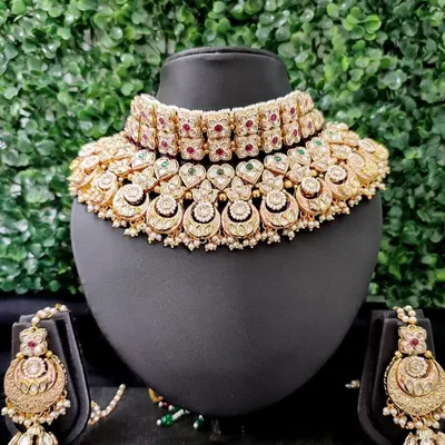 A quintessential bridal choker set in kundan style, featuring half-moon motifs and accented with red and green stones. This is a timeless piece available for rent.