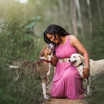 The pure, uncomplicated love between a woman and her dogs. This outdoor portrait captures a tender moment of connection in a beautiful, natural setting. The soft light filtering through the trees adds a magical quality to this heartwarming scene.
