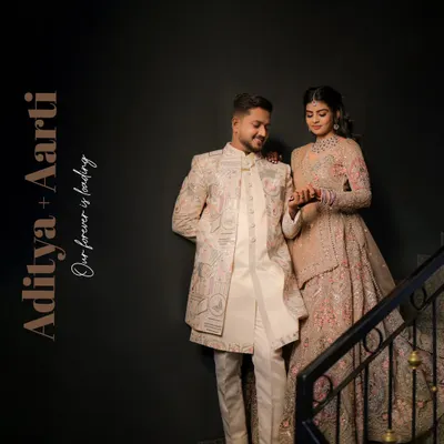 An elegant portrait of a couple in beautifully coordinated ethnic wear, posed on a staircase. The dark background makes their luxurious outfits and connection stand out.