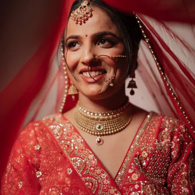A radiant close-up of a bride, her joyful smile captured from under her red veil. This shot beautifully highlights her happiness and traditional bridal jewelry.