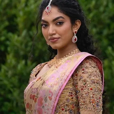 A portrait of a bride in her custom ensemble. The heavily embellished zardozi blouse perfectly complements the soft pink and gold tones of her floral silk saree, creating a look of pure elegance.