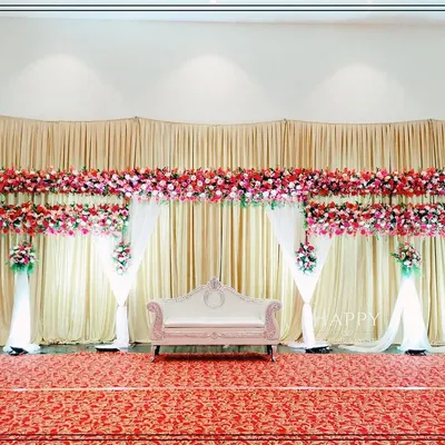 An elegant and budget-friendly stage decoration featuring cream-colored drapes and dense runners of red and pink flowers. This clean and classic design provides a beautiful backdrop without overwhelming the space.